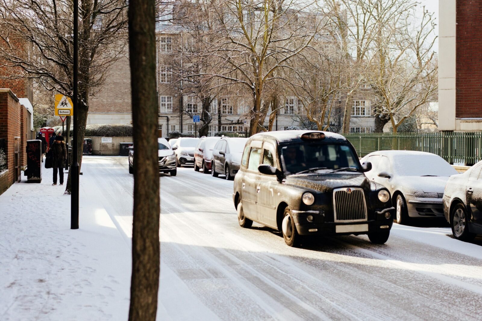 Snowy London street scene with classic black cab and parked cars.