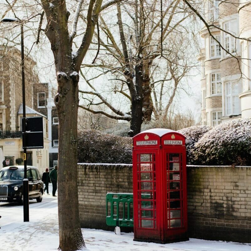 A vintage red telephone booth amidst a snowy street in London, England.